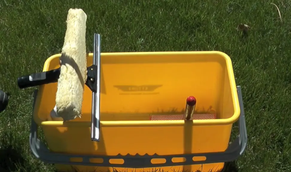 Window scrubber and squeegee in a bucket Yellow bucket holding a window scrubber and a squeegee on the grass