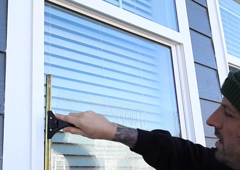 Squeegeeing a window dry Window cleaner pulling a squeegee down a white-framed window on a house with blue siding