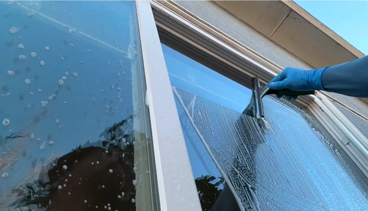 Gloved hand pulling a squeegee across a soapy window