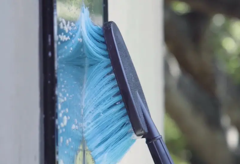 Scrubbing glass with a brush on a pole Soft blue brush on a pole scrubbing soapy water across window glass