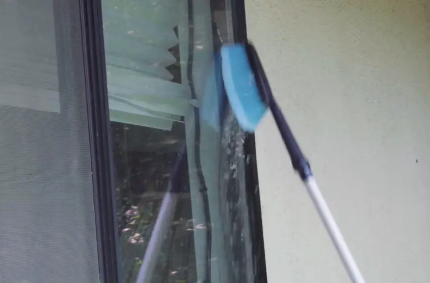 Brush on an extension pole cleaning a window Blue brush on an extension pole scrubbing a window with blinds behind the glass