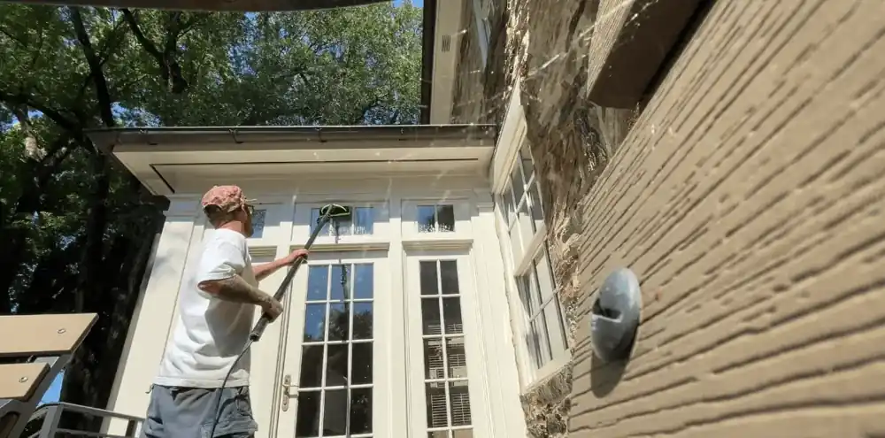 Awbrey Butte window washers Window cleaner using a long pole to clean upper glass above French doors on a stone home