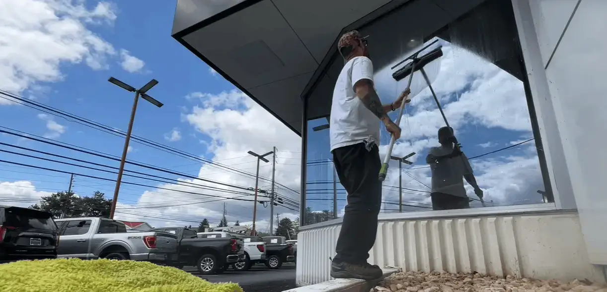 Window cleaner using a long pole and squeegee on tall glass windows under a blue sky